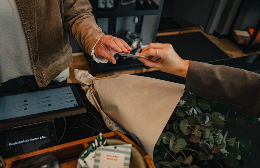 Person übergibt eine Karte an die Kasse, während eine andere Hand sie entgegennimmt.