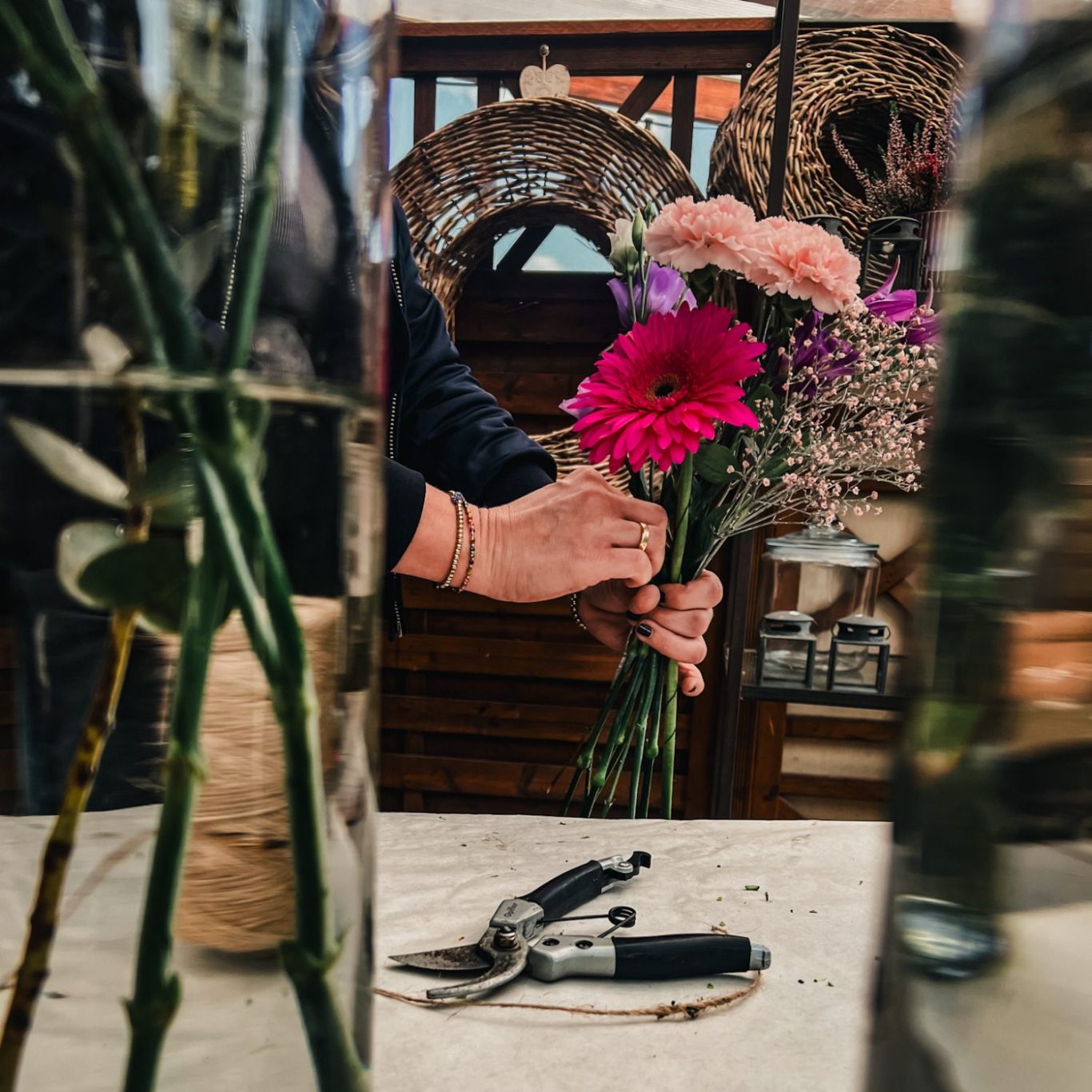 Eine Hand hält einen Strauß mit bunten Blumen zwischen Vasen und Werkzeug.