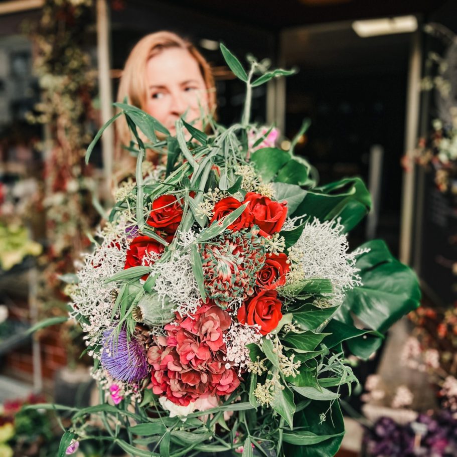 Frau hält einen üppigen Blumenstrauß mit roten Rosen und grünen Blättern.