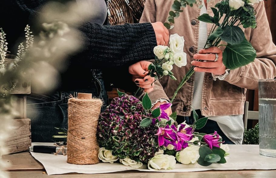 Hände binden Blumensträuße mit verschiedenen Blumen und einer mit Schnur umwickelten Rolle.