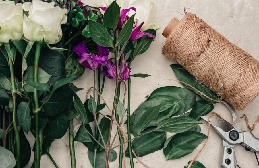 Blumen, Bindfaden und eine Gartenschere auf einer Tischoberfläche.